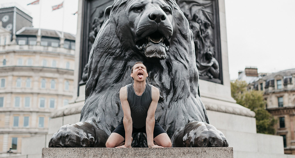 Yogibanker Scott Robinson performing the lion's breath pose in front a statue of a lion
